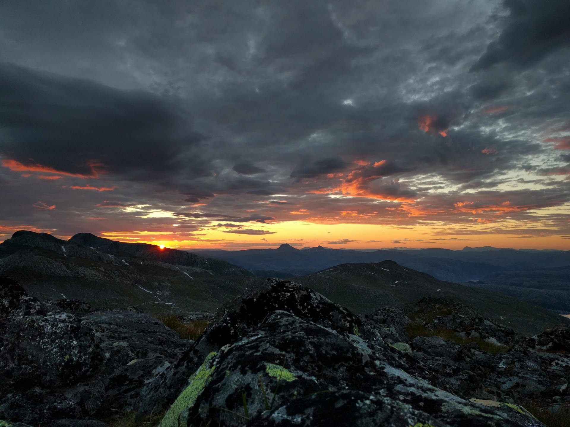 Dramatisk solnedgang over fjellkjeder med steinete forgrunn