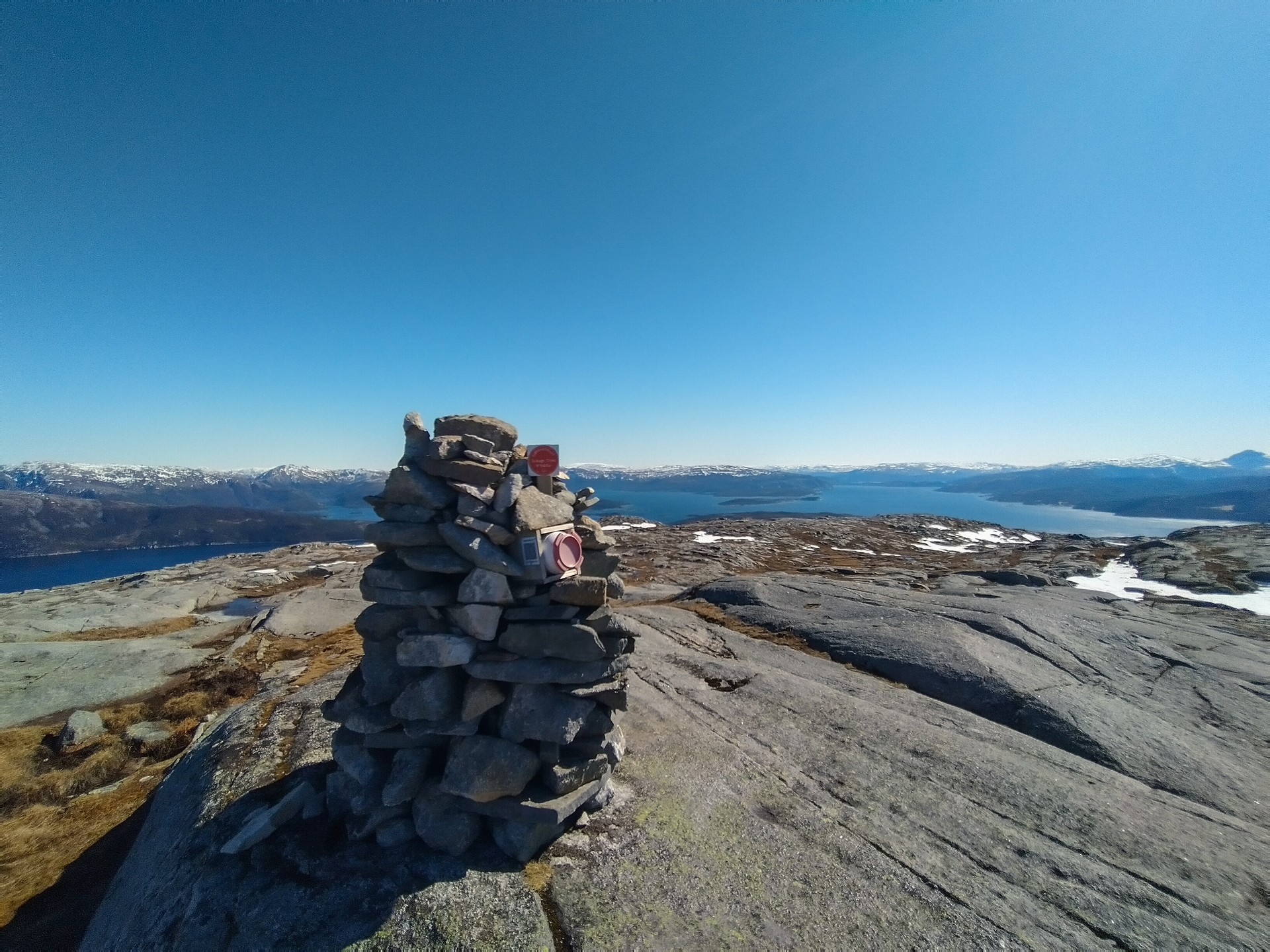 Steinvarde på fjelltopp med utsikt over blå fjorder og snøfjell