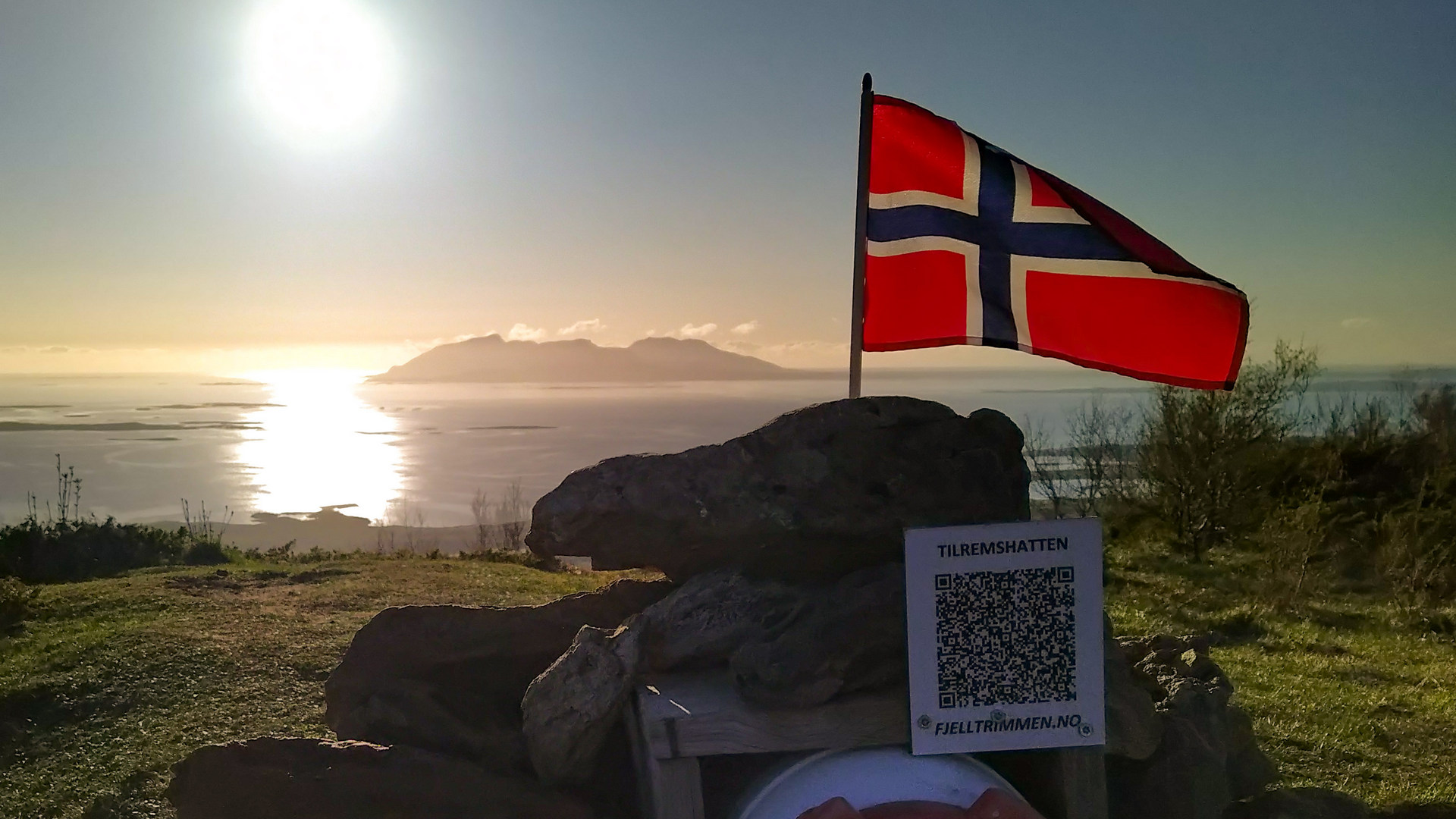 Norsk fjell med flagg og solnedgang over fjorden