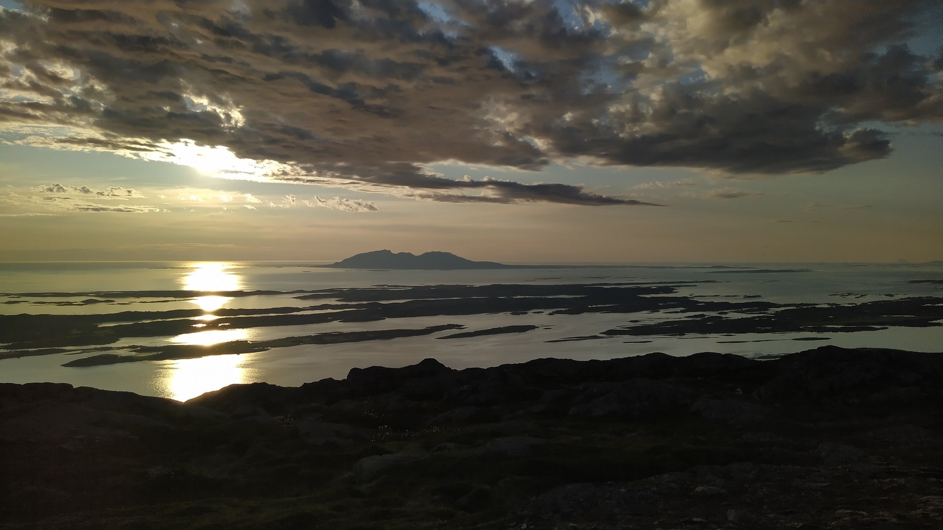 Solnedgang over øysamfunn og fjell ved kysten